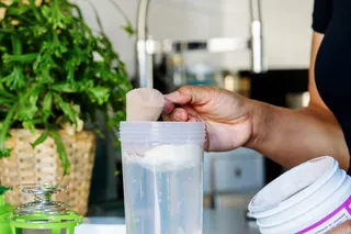 person scooping protein powder into a shake 