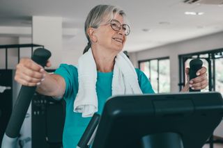 Older woman exercising on an elliptical machine, representing safe physical activity for people with high blood pressure.