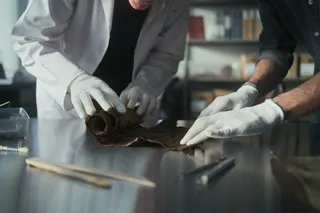 Researchers with gloved hands examining an old scroll 