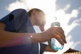 A person holds a water bottle in bright sun during extreme heat, highlighting hydration and heat wave safety.