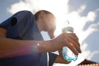 A person holds a water bottle in bright sun during extreme heat, highlighting hydration and heat wave safety.