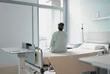 Patient sitting on a bed and looking out of a hospital window 