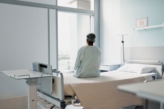 Patient sitting on a bed and looking out of a hospital window 