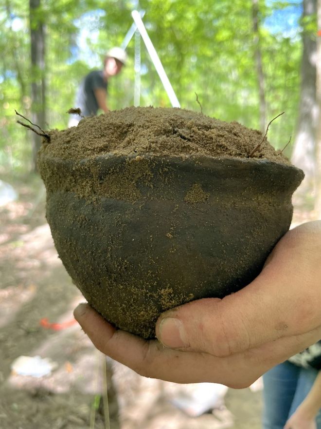 Ancient pot filled with dirt being held up by a human hand 