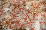 Red Huashan rock paintings of human figures, animals, and circular symbols cover a weathered limestone cliff in southern China.