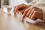 Person taking supplements with a glass of water, could be vitamin D