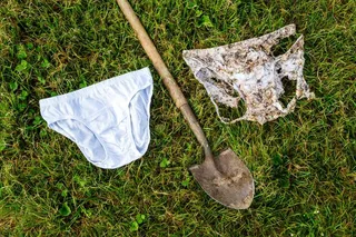 A clean white pair of cotton underwear next to a garden shovel and a badly decomposed, soil-stained pair after two months buried underground