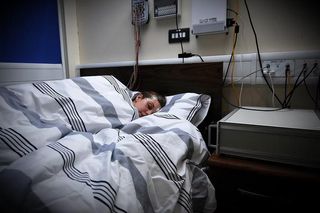 A participant sleeps in a bed with EEG sensors attached to their scalp during a brain and memory study.