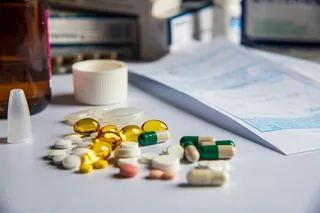 White tablets, green-and-white capsules, and golden softgels scattered beside medicine bottles and paperwork.