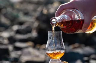 Person pouring whiskey into a glass outside