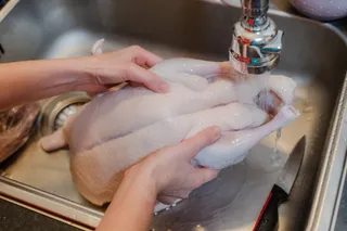 person washing a whole raw chicken